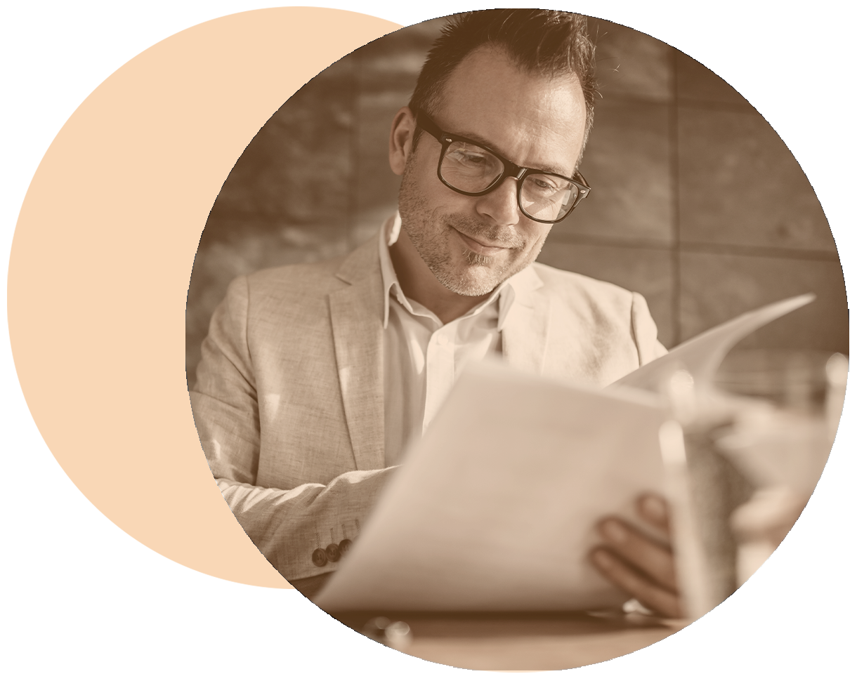 A man in a suit half smiling looking at papers, potentially a business report, with an orange circle shape partially framing the image.
